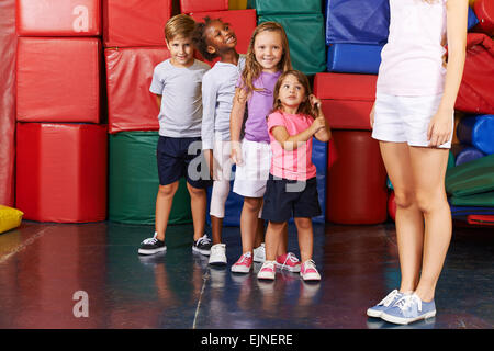 I bambini in piedi in una fila in una palestra della scuola materna con PE insegnante Foto Stock