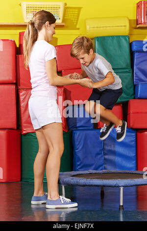 Ragazzo di saltare sul trampolino in palestra con aiuto del maestro di PE Foto Stock