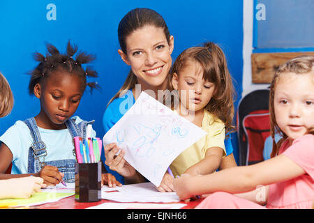 Vivaio insegnante con molti bambini che mostra un disegno in una scuola materna Foto Stock