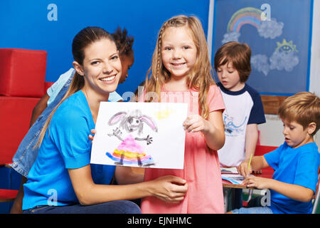 Felice ragazza che mostra la sua immagine dipinta in asilo nido accanto al vivaio insegnante Foto Stock