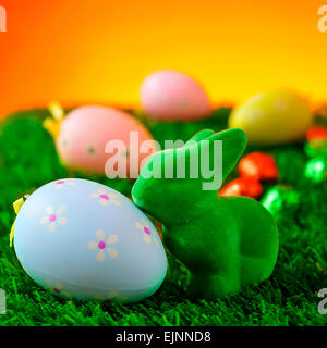Primo piano di un verde il Coniglio di Pasqua e un fiore blu con fantasie di uova di pasqua in erba con alcune decorazioni colorate le uova in b Foto Stock