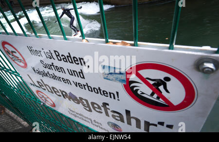 Monaco di Baviera, Germania. 29 Mar, 2015. Un uomo naviga con la sua tavola da surf su un onda nel fiume Eisbach nonostante le avvertenze urgenti da un segno su una barriera che legge 'Il nuoto, surf e kayak vietato - pericolo mortale!' nel Giardino Inglese a Monaco di Baviera, Germania, 29 marzo 2015. Foto: Peter Kneffel/dpa/Alamy Live News Foto Stock