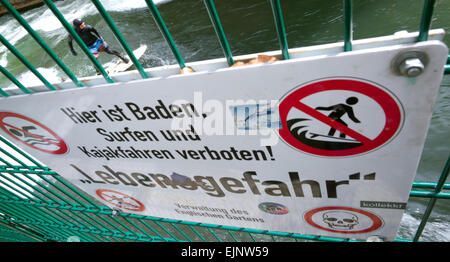 Monaco di Baviera, Germania. 29 Mar, 2015. Un uomo naviga con la sua tavola da surf su un onda nel fiume Eisbach nonostante le avvertenze urgenti da un segno su una barriera che legge 'Il nuoto, surf e kayak vietato - pericolo mortale!' nel Giardino Inglese a Monaco di Baviera, Germania, 29 marzo 2015. Foto: Peter Kneffel/dpa/Alamy Live News Foto Stock