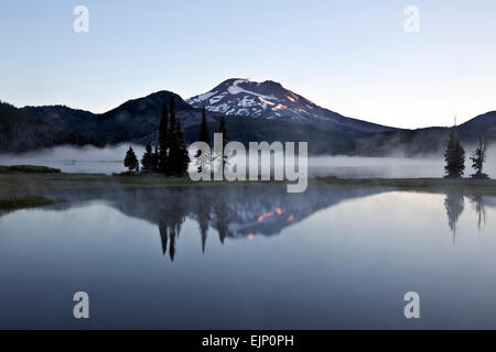 OREGON - nebbia scintille sul lago e una riflessione del Sud sorella nella nebbia a sunrise in Deschutes National Forest. Foto Stock