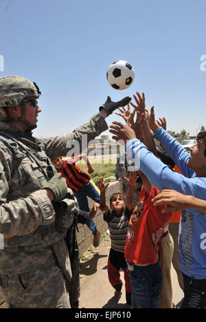 Un U.S. Soldato da Echo Company, 1° Battaglione, 8° reggimento di cavalleria, 2° Brigata pesante Team di combattimento, 1° Divisione di cavalleria, Fort Hood in Texas, lanci di un pallone da calcio a un gruppo di ragazzi iracheni nel villaggio di Ka bashe a Kirkuk, Iraq, 31 maggio. Negli Stati Uniti le forze di coalizione partner con la polizia irachena per ispezionare i sistemi di irrigazione e di incontro con gli agricoltori locali che hanno l'agricoltura riguarda in e intorno alla città di Kirkuk provincia dell'Iraq. Foto Stock