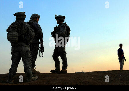 Stati Uniti I soldati dell esercito guardia mentre un iracheno uomo orologi della distanza come il sole tramonta all'inizio di una pattuglia durante il funzionamento Magnon al-Wombet in Shaab, Iraq, 10 aprile 2009. Il funzionamento è stato progettato per arrestare il flusso di ordigni esplosivi artigianali, armi ed il contrabbando dalla periferia della città nel suo centro. I soldati sono assegnati alla truppa e 1° Battaglione, quinto reggimento di cavalleria. Il personale Sgt. Contrassegnare Burrell Foto Stock