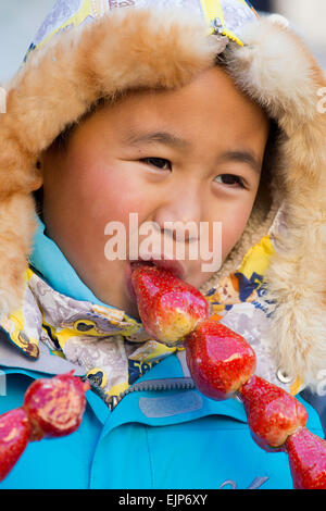 Cina, Provincia di Heilongjiang, Harbin, inverno, ragazzo di mangiare frutta congelata Foto Stock