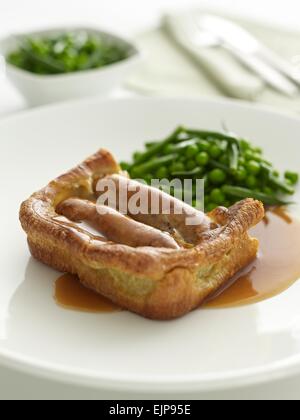 Pasto placcati di rospo nel foro Yorkshire pudding e salsicce con sugo di piselli e fagiolini Foto Stock