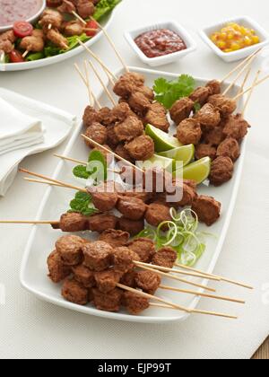 A buffet piatto di pollo a pezzi su spiedini di legno con un peperoncino dolce dip lattuga e pomodori menta lime pezzi Foto Stock