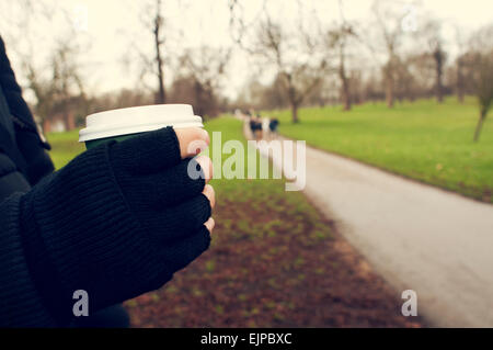 Primo piano di un giovane uomo caucasico molto al riparo indossando guanti senza dita mantiene una bevanda calda in un bicchiere di carta in Hyde Park in inverno Foto Stock