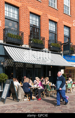 Uomo che cammina passato i clienti seduti fuori la Cote Brasserie in Exeter Foto Stock