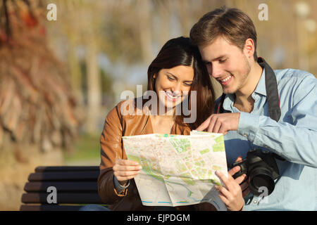 Felici i turisti alla ricerca dei punti di riferimento in una mappa seduta su una panchina all'aperto Foto Stock