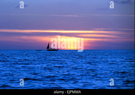 Una barca a vela si stagliano contro una vivida Cielo di tramonto. Foto Stock