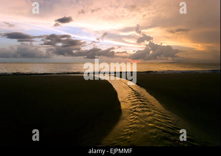 Una scintillante torrente scorre in un oceano bellissimo tramonto con un cielo nuvoloso al di là. Foto Stock