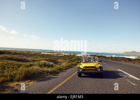 Coppia giovane guida lungo una strada aperta entusiasta di essere su un roadtrip. Coppia felice alla guida di una vettura con le braccia alzate. Foto Stock