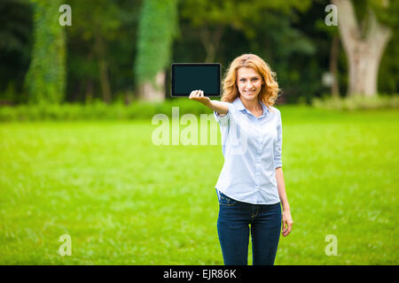 Giovane bella donna con tavoletta in mano, nel camminare nel parco Foto Stock