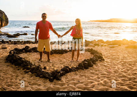 Giovane tenendo le mani a forma di cuore sulla spiaggia Foto Stock