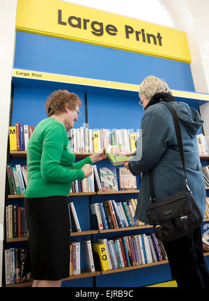 Un bibliotecario aiuta un cliente a fianco della grande sezione di stampa di libri Foto Stock