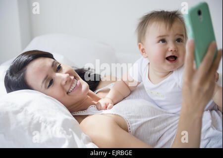 Razza mista madre giocando con il bambino e il telefono cellulare sul letto Foto Stock