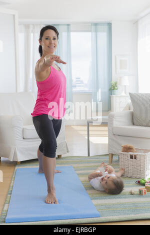 Razza mista madre a praticare yoga e guardare il bambino a casa Foto Stock