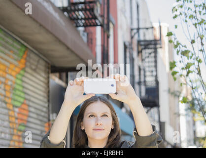 La donna caucasica tenendo il telefono cellulare la fotografia sul marciapiede urbano Foto Stock