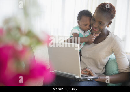 Nero madre e figlio utilizzando computer portatile sul divano Foto Stock