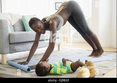 Madre nera la pratica dello yoga con baby boy in salotto Foto Stock