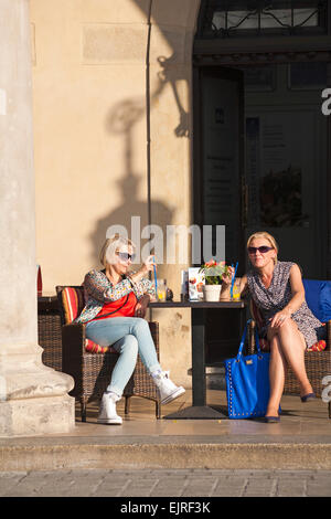 Coppia di donne al di fuori seduta gustando un drink nella piazza principale del mercato, Cracovia in Polonia nel mese di settembre Foto Stock