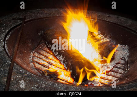 Un incendio si illumina brillantemente in un firepit con un poker di appoggio sul lato. Le ceneri e le braci sono visibili. Foto Stock