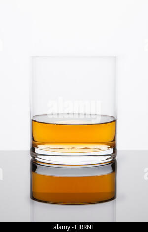 Rocce di un vetro con il Whisky si siede in cima ad una superficie riflettente su uno sfondo bianco Foto Stock