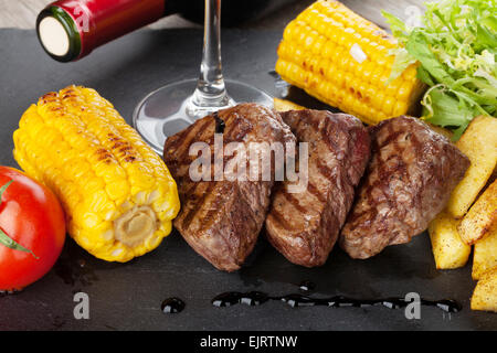 Bistecca alla griglia con patate, mais, insalata e vino rosso closeup Foto Stock