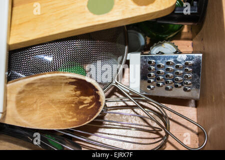 Vari utensili da cucina in un cassetto con un cucchiaio di legno, il crivello inferiore un mini Grattuggia formaggio, frusta e tappi di bottiglie. Foto Stock