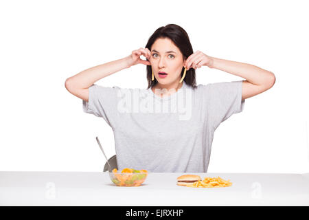 Naturale donna espressiva giocando con patatine fritte, avendo di fronte junk e cibo sano, isolato su bianco Foto Stock