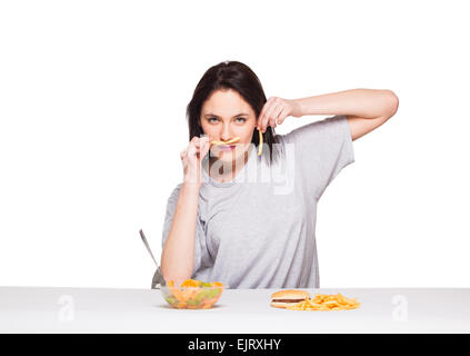 Naturale donna espressiva giocando con patatine fritte, avendo di fronte junk e cibo sano, isolato su bianco Foto Stock