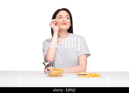 Naturale donna espressiva giocando con patatine fritte, avendo di fronte junk e cibo sano, isolato su bianco Foto Stock