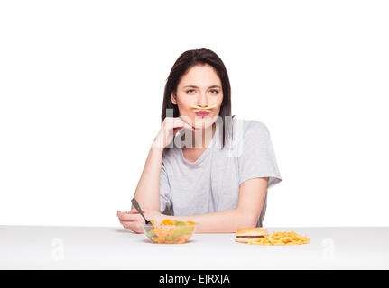 Naturale donna espressiva giocando con patatine fritte, avendo di fronte junk e cibo sano, isolato su bianco Foto Stock