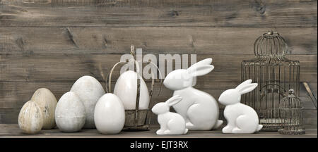 Conigli pasquali e uova su legno rustico sfondo. In stile retrò decorazione con birdcage. Vintage foto dai toni Foto Stock