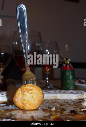 Una forcella in uno avanzi di patate arrosto da un pasto di Natale con mezzo pieno bicchieri di vino e una tirata cracker in background. Foto Stock