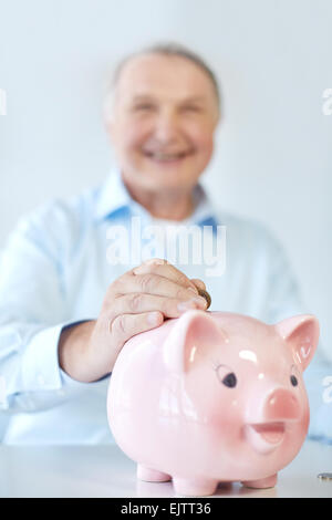 Chiusura del vecchio uomo mettendo una moneta nell piggybank Foto Stock