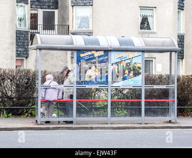 Una coppia di anziani stare sotto un vetro racchiuse in un rifugio in attesa per un autobus di Edimburgo, in Scozia. Foto Stock
