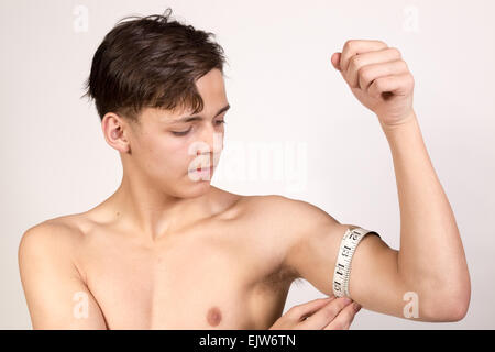 White ragazzo adolescente misurando il suo muscolo bicipite. Studio shot. Foto Stock
