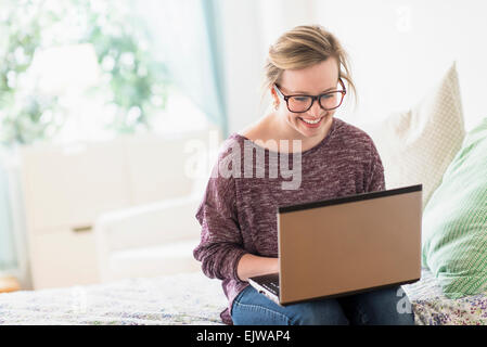 Giovane donna seduta sul letto e utilizzo di computer portatile Foto Stock