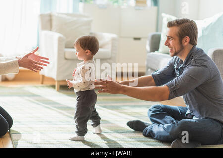 Genitori felici aiutare piccolo figlio (2-3 anni) a piedi nella stanza vivente Foto Stock