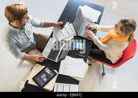 Giovane uomo e donna con computer portatili a scrivania in ufficio Foto Stock