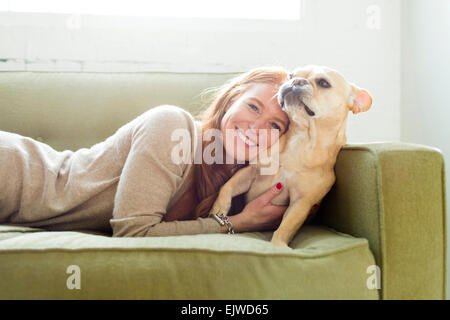 Donna sdraiata sul divano abbracciando pug Foto Stock
