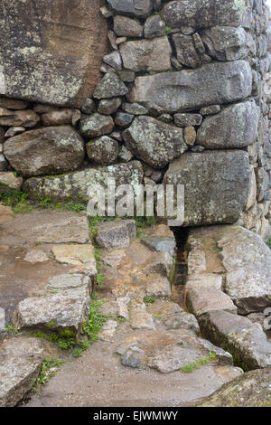 Il Perù, Machu Picchu. Canal portando acqua da una primavera in montagna all'interno della città, passando sotto la parete esterna. Foto Stock