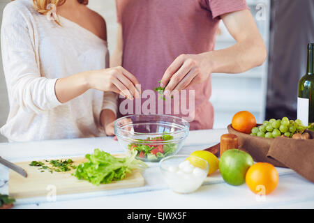 Le mani della coppia giovane aggiungendo prezzemolo tagliato nella ciotola con fresche insalate vegetariana Foto Stock