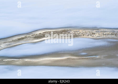 Flusso di riflessione d'oro l'acqua che scorre al di sotto di uno strato di neve nella stagione invernale Foto Stock