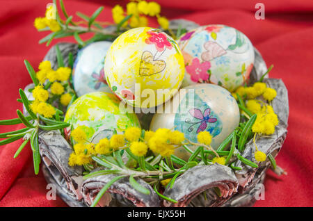 Cesta piena di colorati a mano le uova di Pasqua in decoupage contro uno sfondo rosso Foto Stock