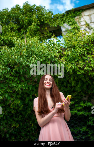 Donna che utilizza il telefono verde sullo sfondo di edera Foto Stock